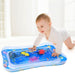 A baby in a white onesie crawls on a blue inflatable water mat with colorful floating toys.