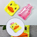 A yellow duck hot water bottle cover and a separate pink plastic hot water bottle on a grey surface.