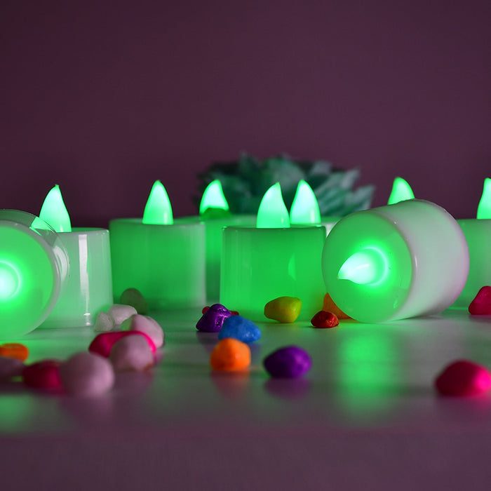 Several green flameless LED tealights are arranged on a surface with colorful pebbles, one tealight is on its side.