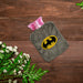 Gray plush hot water bag with a Batman logo on a dark wooden surface with white flowers and green leaves.