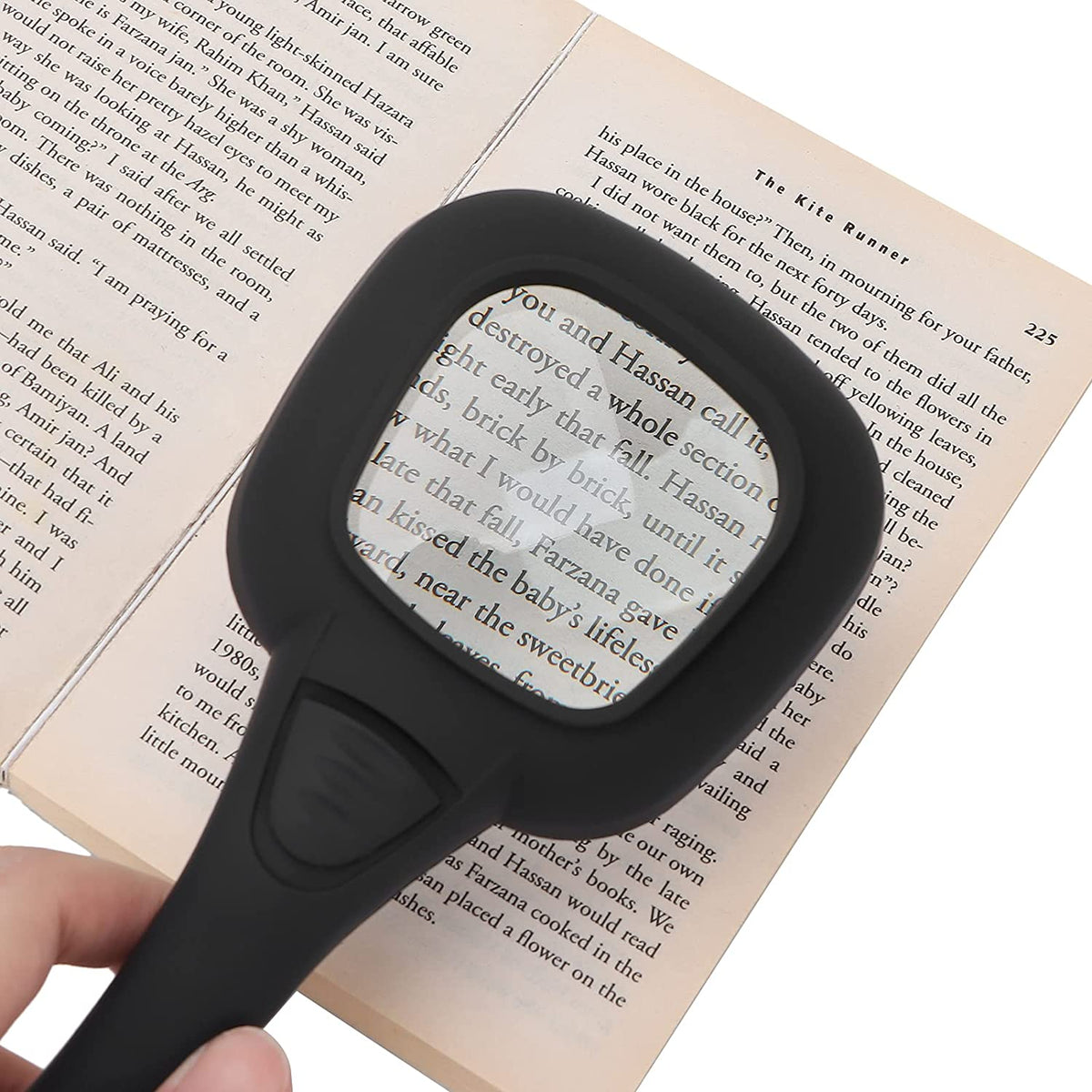 A hand holds a black magnifying glass over an open book, showing magnified text through the lens.