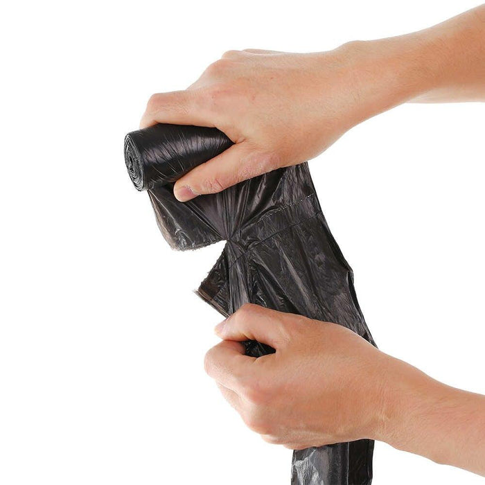 Hands unrolling and tearing off a single black garbage bag from a roll.