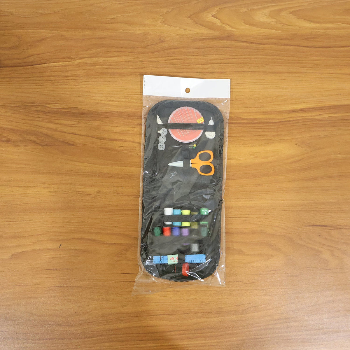 A packaged black zippered sewing kit, containing colorful threads and tools, is sealed in clear plastic and displayed on a