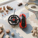A red remote control car and its steering wheel controller sit on a playmat with toy blocks and other small cars.