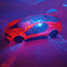 A red remote control car with a clear roof projects blue and red lights onto a dark surface.