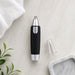 A black and silver nose hair trimmer with its clear cap removed lies on a white marble surface next to a white towel and