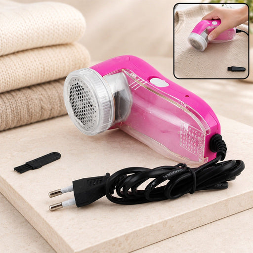 Pink corded lint remover with a cleaning brush and power plug on a light surface with folded sweaters.
