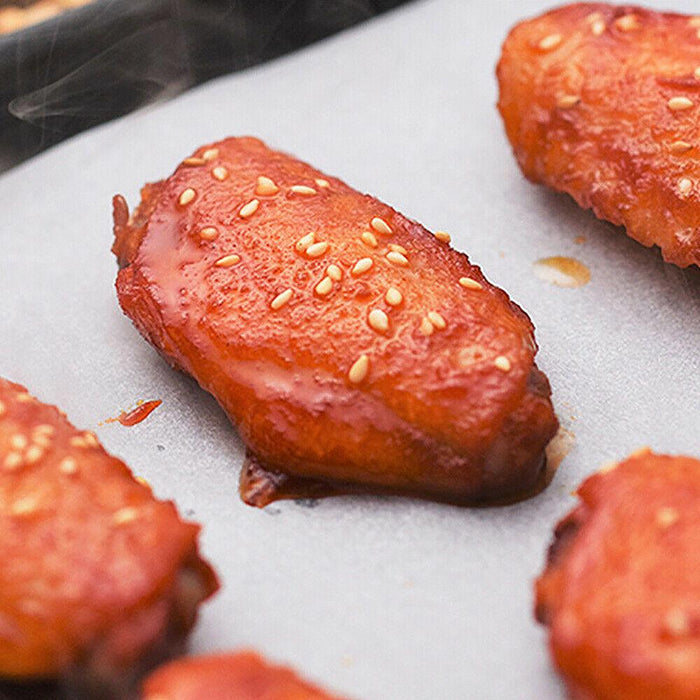 A close-up of a glazed chicken wing with sesame seeds on a sheet of white baking paper.