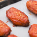 A close-up of a glazed chicken wing with sesame seeds on a sheet of white baking paper.
