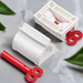 Two white plastic tube squeezers and a detached red winding key are displayed on a grey surface with green leaves.