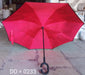 An open, bright red reverse umbrella with a C-shaped handle is displayed on a concrete floor in a warehouse setting.