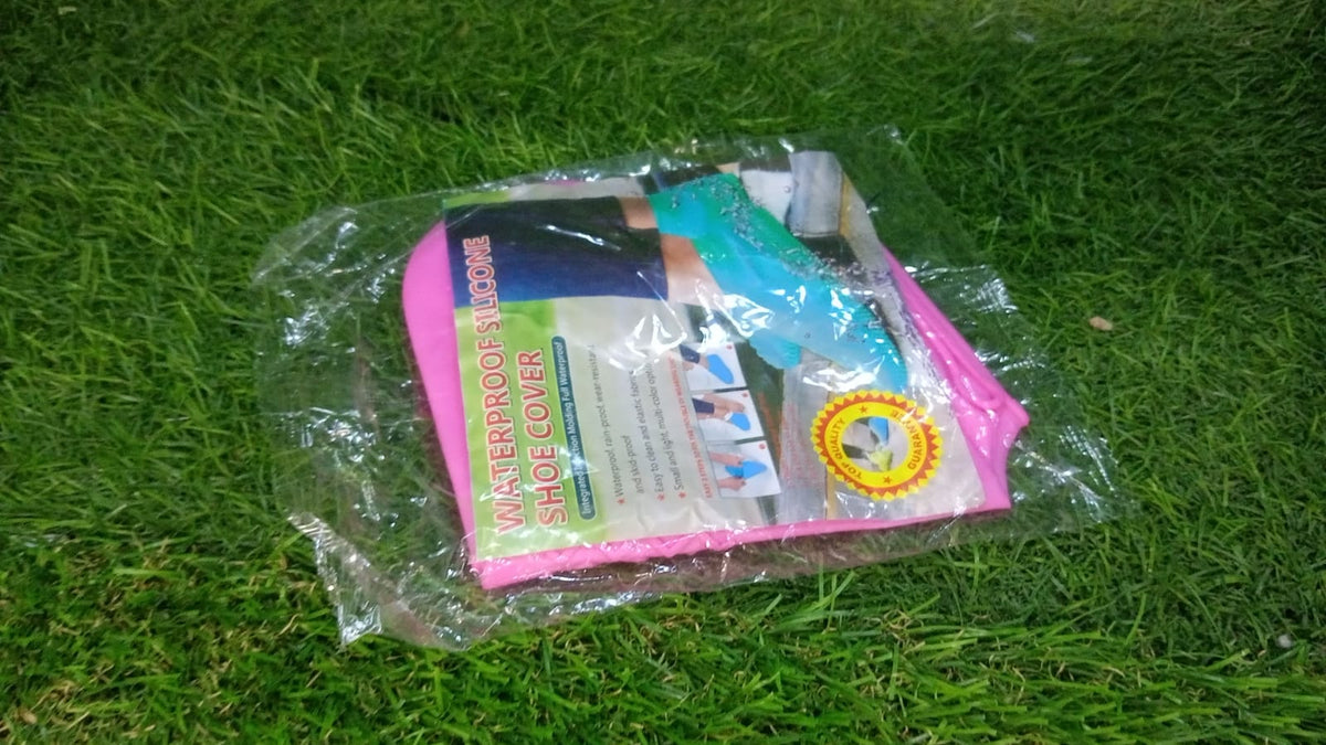 A clear plastic package containing pink silicone shoe covers, lying on green grass.