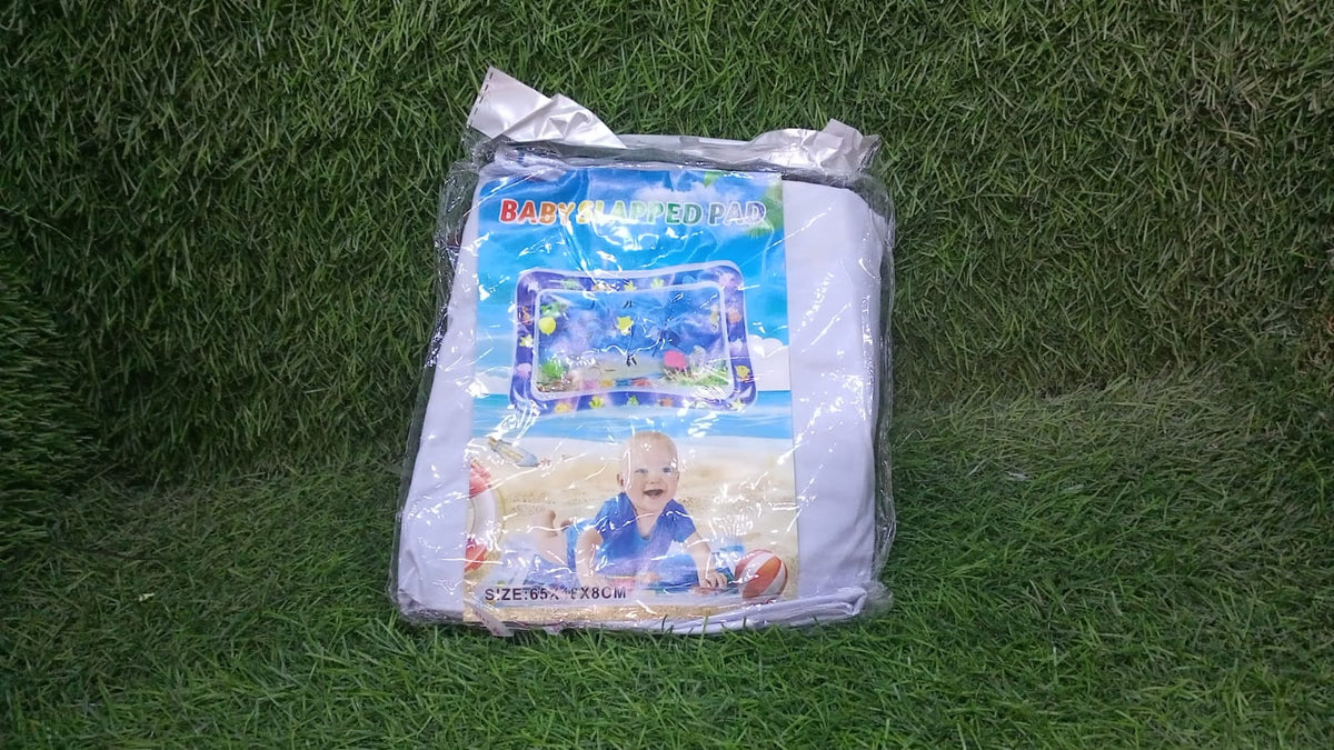 A packaged baby water play mat with a picture of a baby on it, lying on green grass.