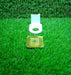 A white plastic bottle holder and a metallic adhesive pad are displayed separately on a vibrant green artificial grass